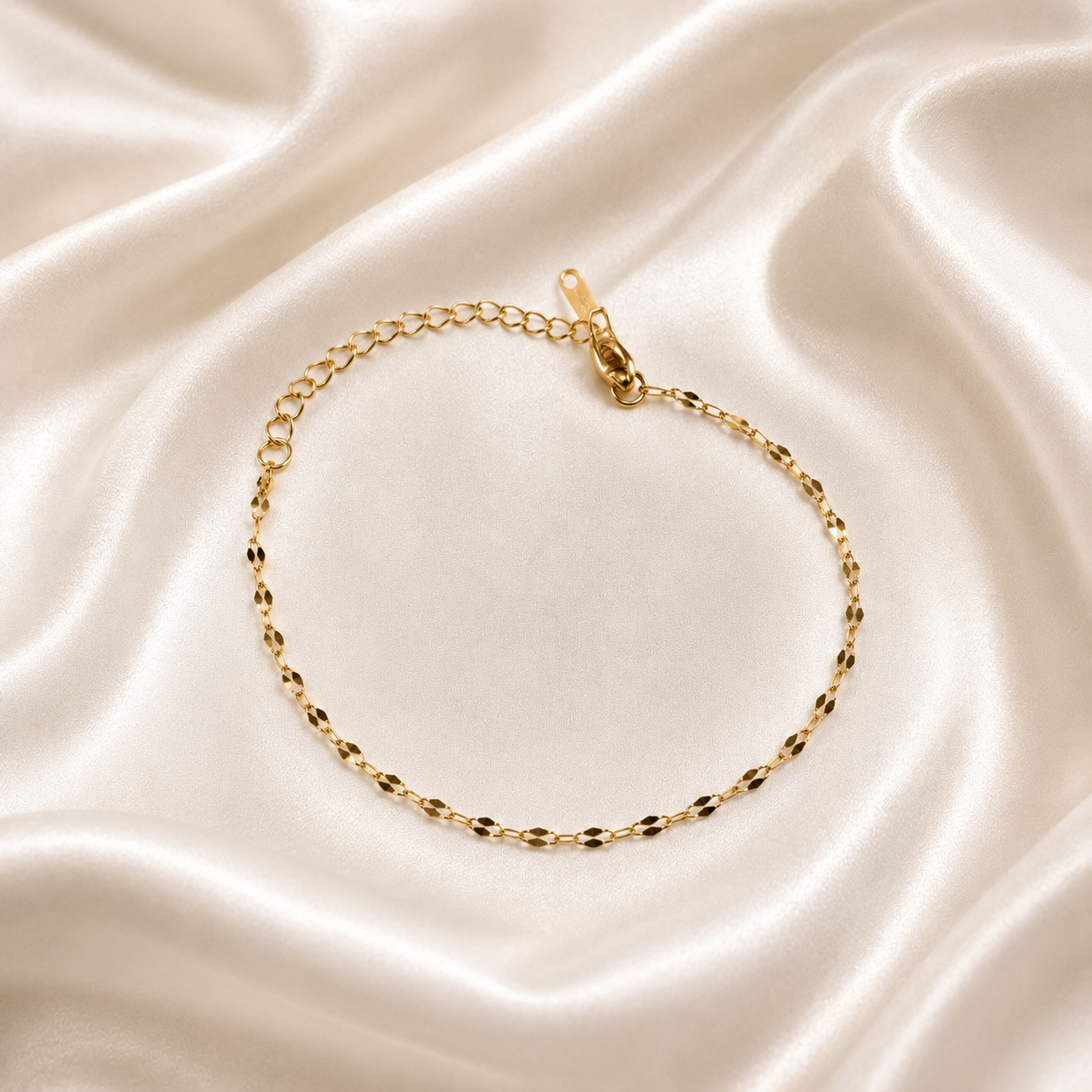 A delicate gold tonned chain bracelet with a lobster clasp, displayed on a draped cream satin fabric background.