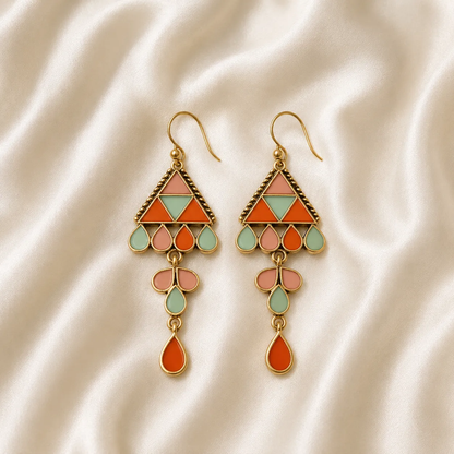 A pair of bohemian-style dangle earrings with gold-tone metal and colorful enamel details, displayed on a draped cream satin fabric background.