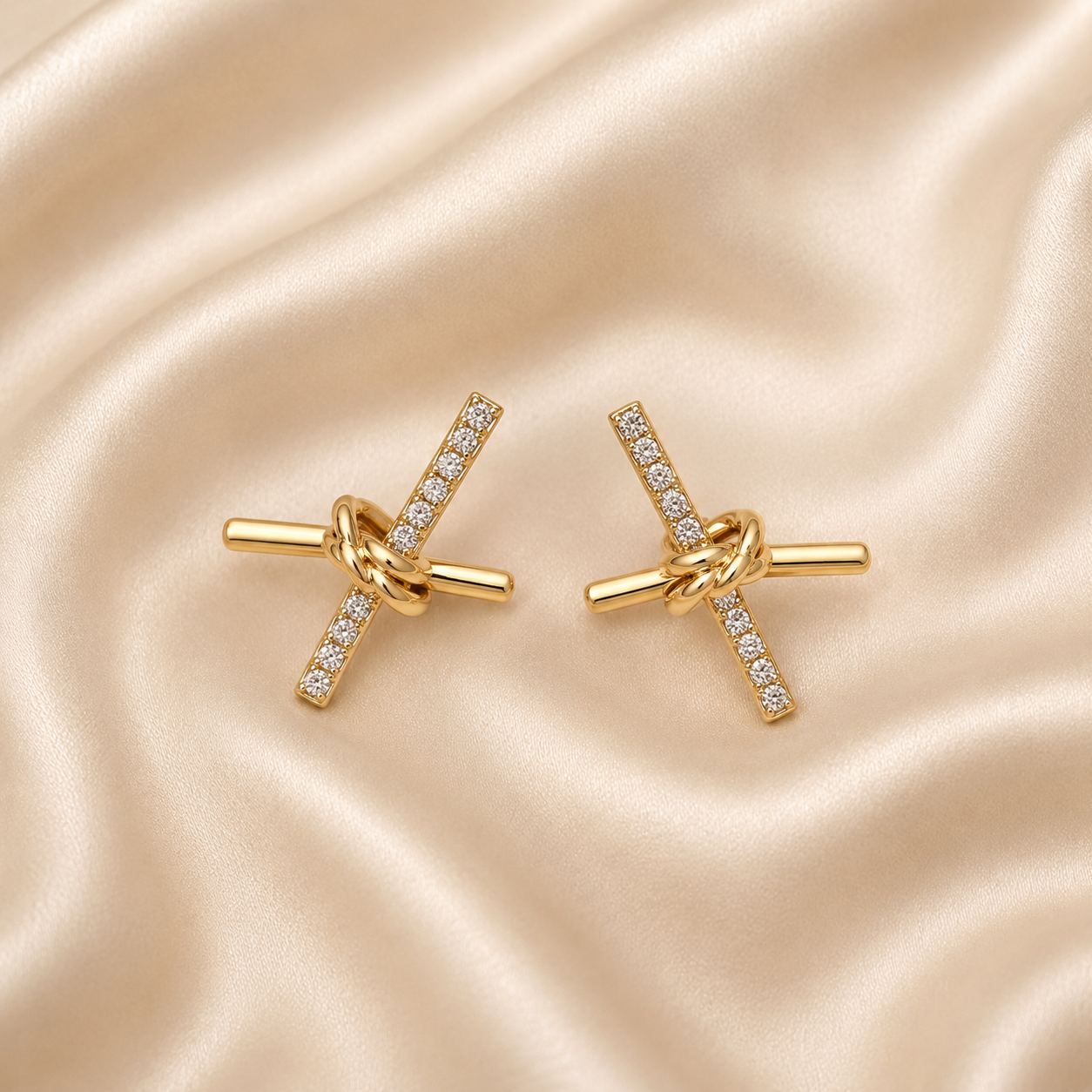 A pair of gold toggle-style cufflinks with diamond-set bars and a knotted center detail, displayed on a draped champagne satin fabric background.