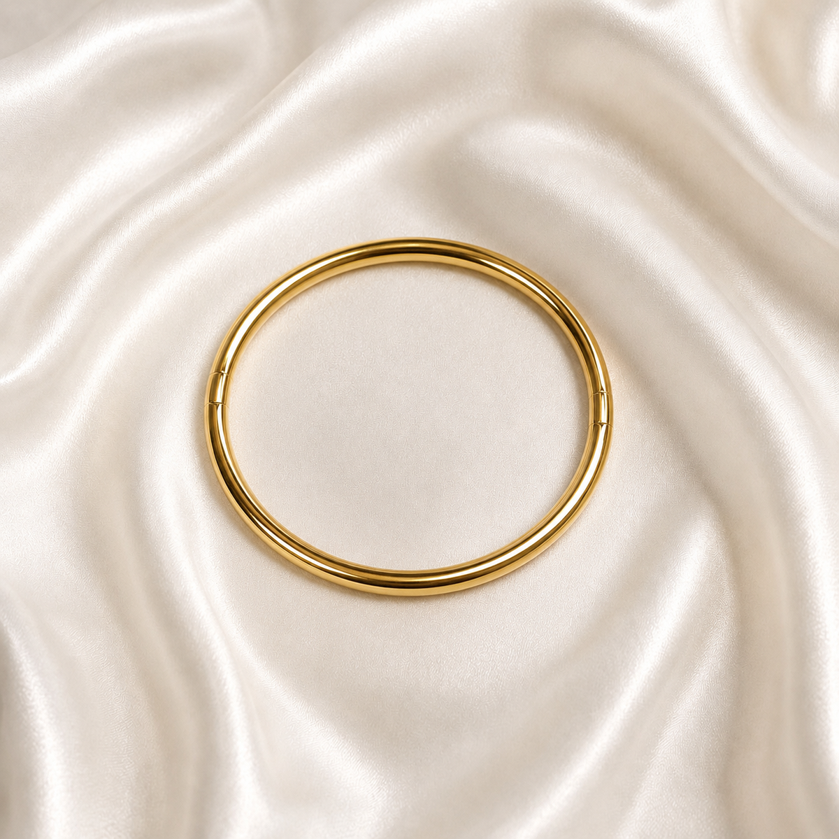 A polished gold tonned bangle bracelet displayed on a draped cream satin fabric background.