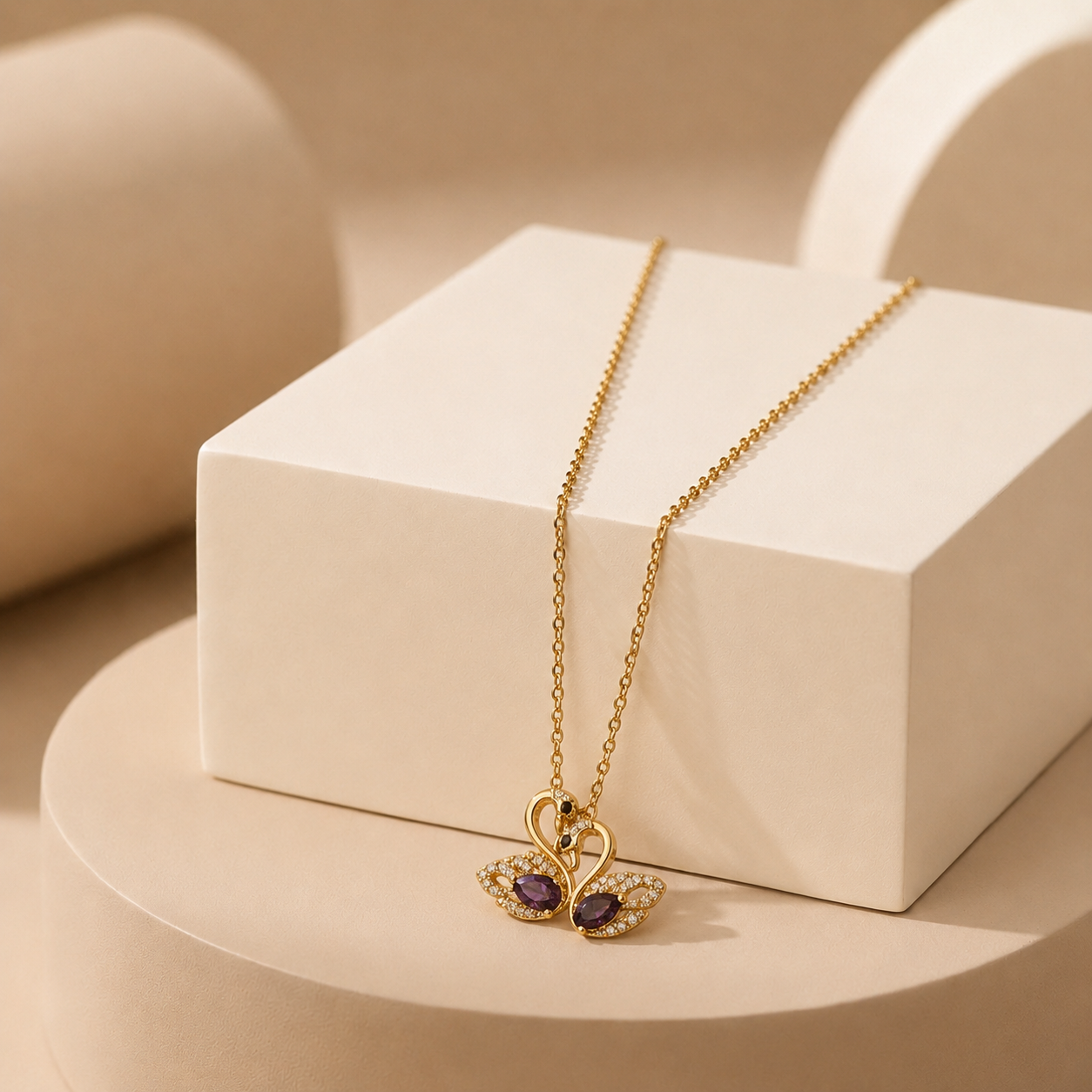 A gold-tone amora teddy anti tarnish necklace with a butterfly pendant featuring purple gemstones and small clear stones, displayed on a white geometric block against a warm beige studio background.