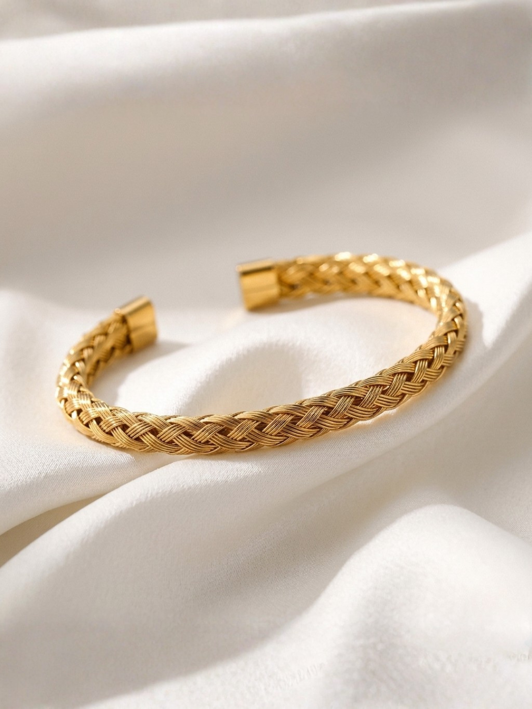 Gold tonned aurora braided bracelet on a white fabric background