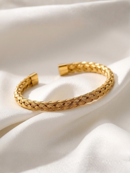 Gold tonned aurora braided bracelet on a white fabric background