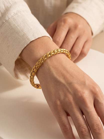 Gold plated braided bracelet on a women's wrist against a neutral background