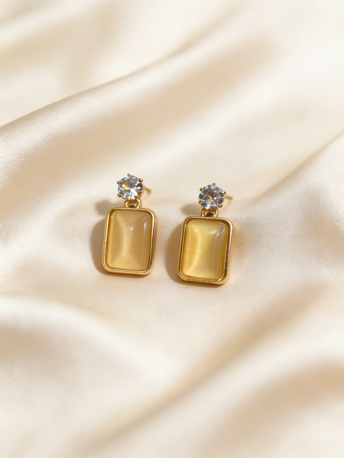 Pair of gold tonned earrings with clear stones on a beige fabric background