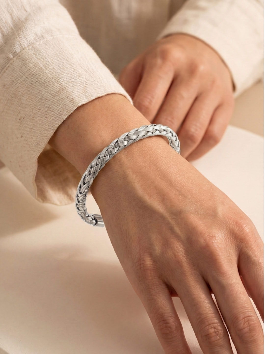 Silver braided bracelet on a women's wrist against a neutral background