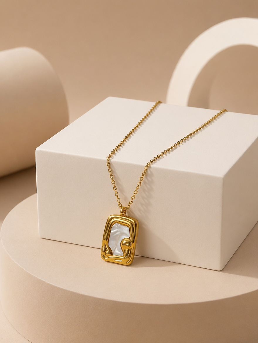 A gold tonned chain necklace with a geometric, open-frame pendant featuring a white inlay, displayed on a white geometric pedestal against a warm beige background.