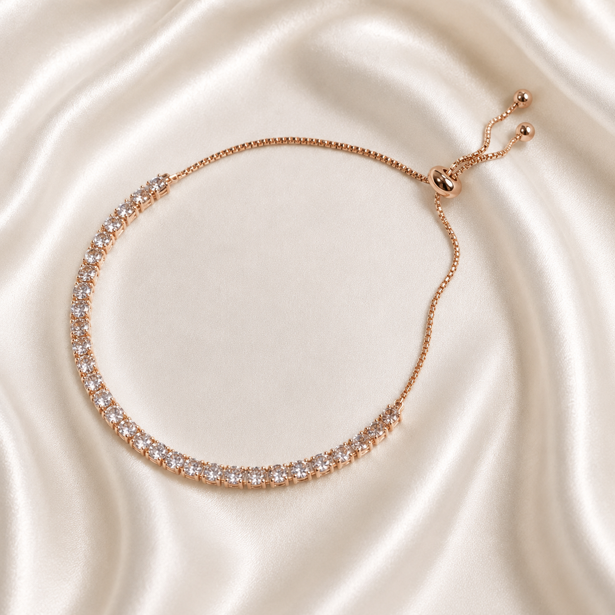 A rose gold tennis bracelet with clear stones, displayed on a draped cream satin fabric background.