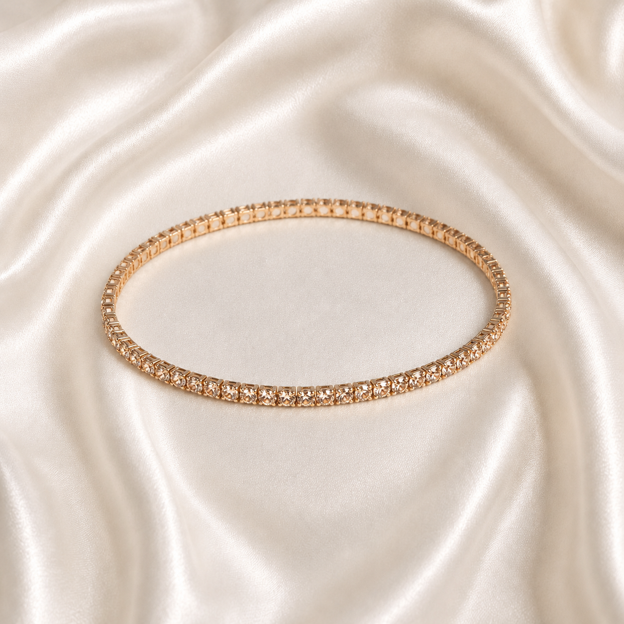 A thin rose gold tonned aura spark bracelet with clear stones, displayed on a draped cream satin fabric background.
