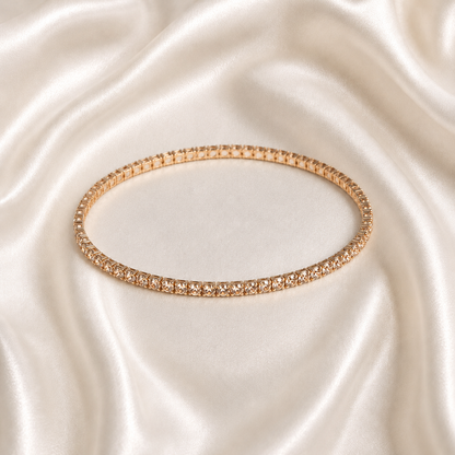 A thin rose gold tonned aura spark bracelet with clear stones, displayed on a draped cream satin fabric background.