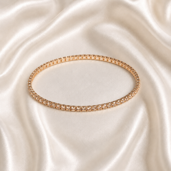A thin rose gold tonned aura spark bracelet with clear stones, displayed on a draped cream satin fabric background.
