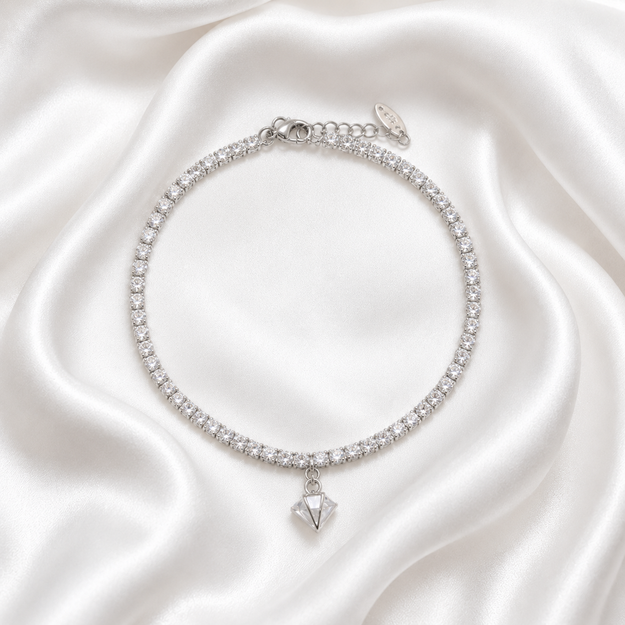 A silver-toned tennis-style choker bracelet adorned with clear cubic zirconia stones and a dangling faceted clear gemstone pendant, displayed on draped white satin fabric.