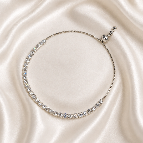 A delicate silver tennis-style necklace with clear sparkling stones, displayed on a draped cream satin fabric background.