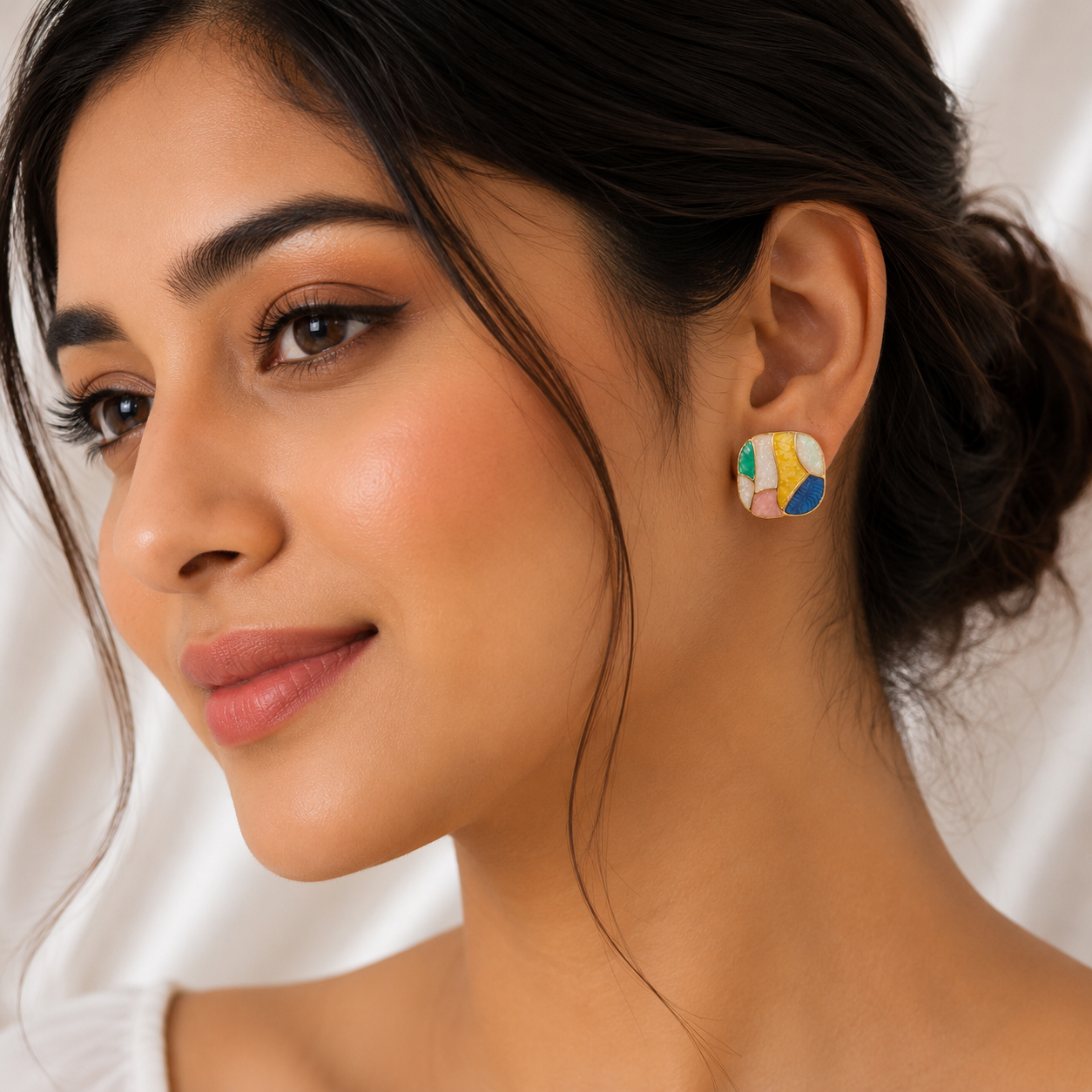 A close-up of a woman wearing a colorful geometric stud earring with abstract shapes in yellow, blue, green, and white.