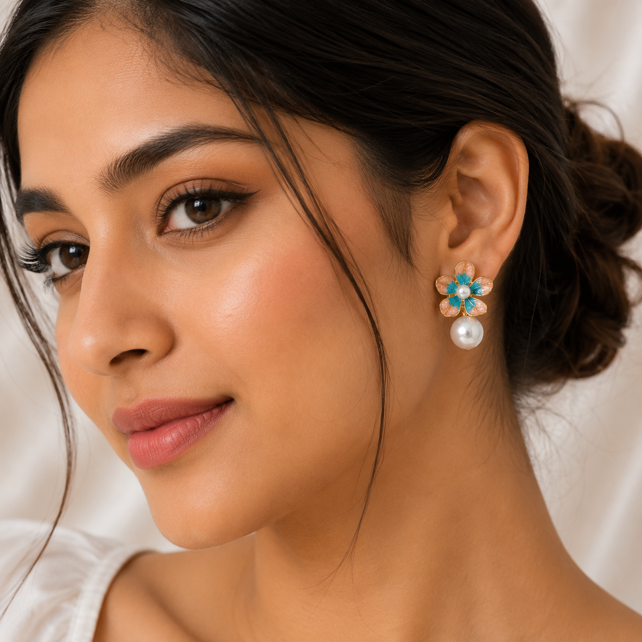 A close-up of a woman wearing a flower-shaped stud earring with turquoise blue stones, rose gold-tonned metal, and a white pearl.