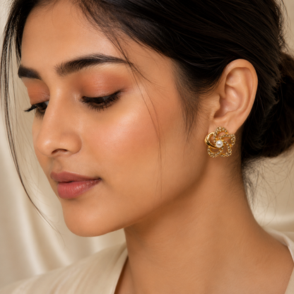A close-up of a woman wearing a gold-toned, flower-like earring with a central pearl, set against a soft cream satin background.