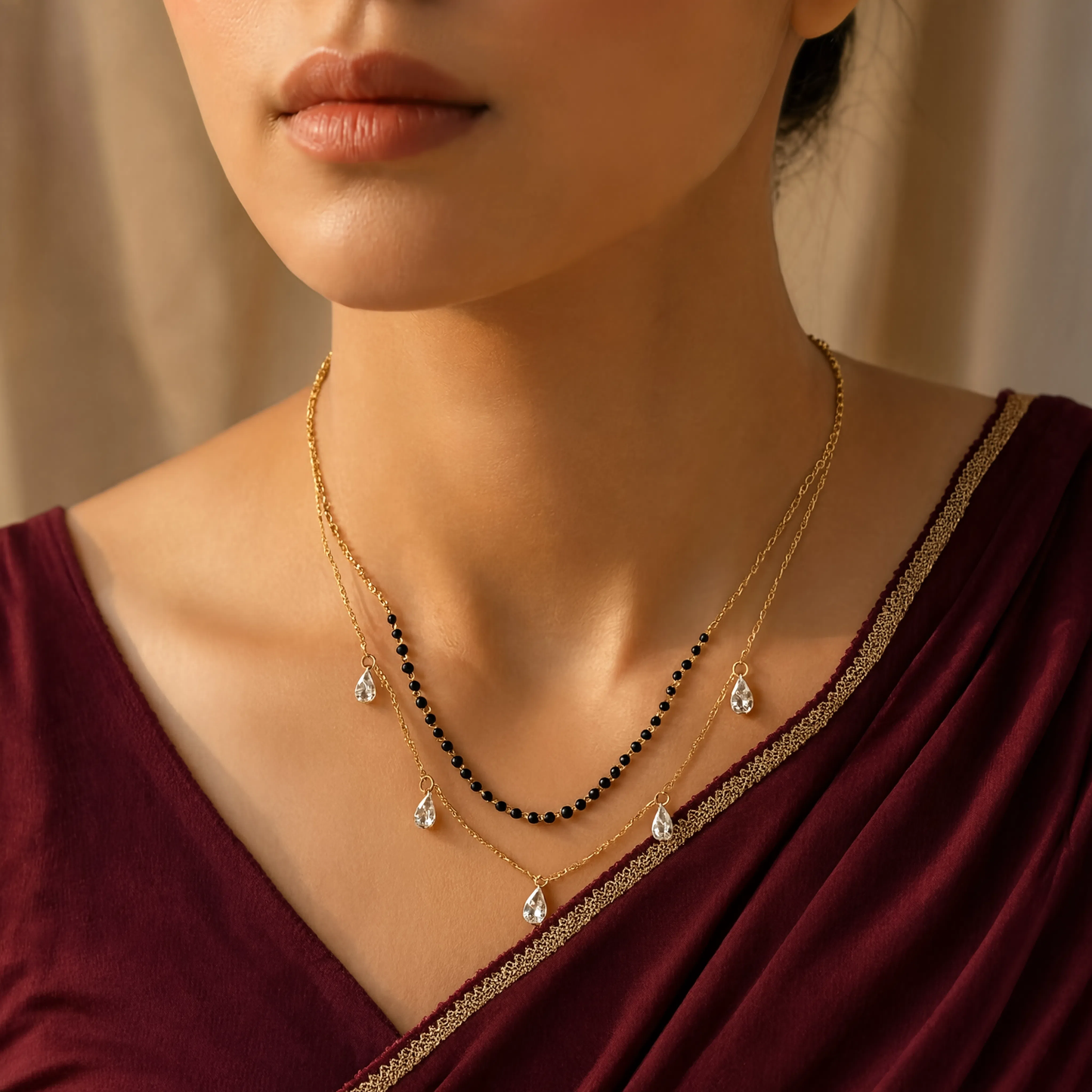 A close-up of a woman wearing a layered gold tonned necklace set with teardrop crystal pendants, one layer featuring small black beads.