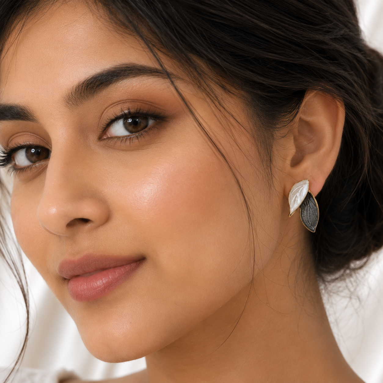 Close-up of a woman wearing a pair of silver-toned leaf-shaped drop earrings, with one earring in front of the other.