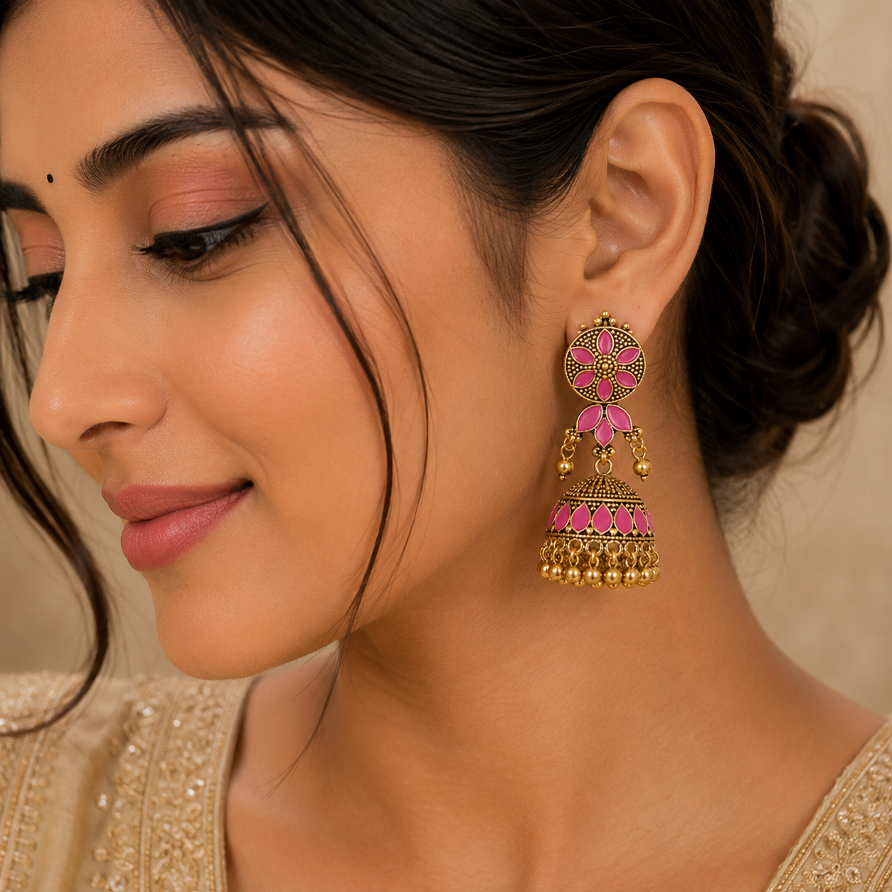 A close-up of a woman wearing a single ornate gold-toned dangle earring with bright pink stone accents, shown against a soft beige background.