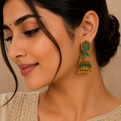 A close-up of a woman wearing a traditional Indian gold-plated dangle earring with green enamel and small red stone accents.